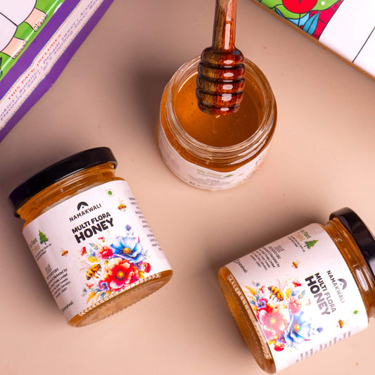 Three jars of honey with a honey dipper on a colorful box background